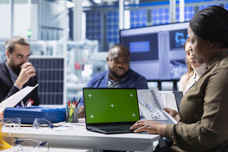 Factory management team look over schematics, planning work using isolated screen laptop. Solar panels plant shareholders look over assembly lines blueprints diagrams, working on mockup notebook